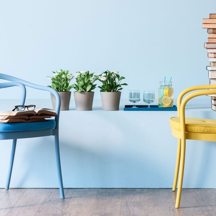 Två färgglada stolar, den ena blå med öppen bok och glasögon, den andra gul, vända mot varandra som en myskrok i en charmig Göteborgs presentbutik. En bunt böcker, krukväxter och en bricka med lemonad sitter på en avsats mot en ljusblå vägg. Det ljusa trägolvet ger värme till scenen.