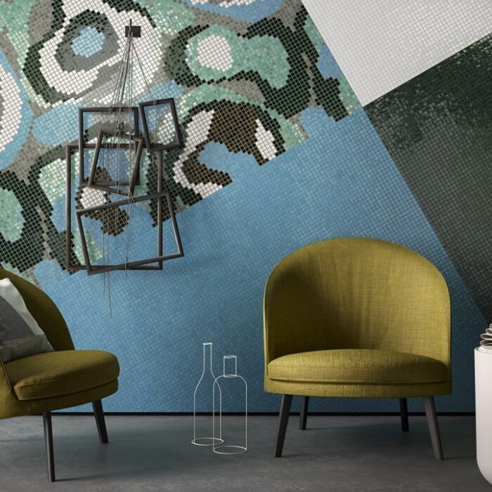 Ett modernt rum med två gröna stolar, ett litet vitt bord med en bok och en modern lampa. Väggen har ett färgstarkt, abstrakt geometriskt mönster i blått, grönt och grått, med en unik fyrkantig ram kanske hämtad från en Göteborgs presentbutik.