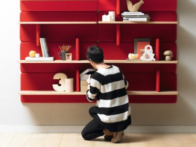 I en svart och vit randig tröja organiserar en individ föremål på en röd väggmonterad hylla. Hyllan, som påminner om en Haga-butik i Göteborg, visar prydnadsföremål, böcker och små föremål. Med sitt trägolv utstrålar scenen en snygg, minimalistisk estetik.