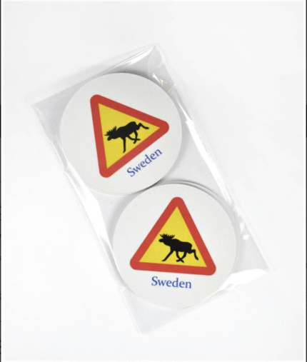 Två cirkulära underlägg med en gul och röd triangulär varningsskylt för älg och ordet "Sverige" tryckt nedanför, förpackade tillsammans i ett genomskinligt plastfodral mot vit bakgrund.