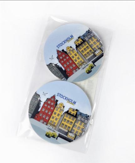 Två runda underlägg med färgglada byggnader i Stockholms stadskärna och texten ”STOCKHOLM” ovanför, placerade i ett genomskinligt plastfodral mot vit bakgrund.