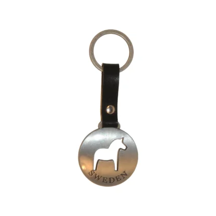 En rund metallnyckelring med en utskuren silhuett av en husky och ordet "SWEDEN" graverat nedanför, fäst vid en svart läderrem och metallnyckelring. Produkt: Husky, längd 25 cm.