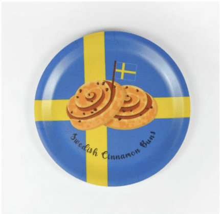 En blå tallrik med ett gult nordiskt kors, som liknar den svenska flaggan, föreställer två kanelbullar och en liten svensk flagga. Texten lyder "Svenska kanelbullar".