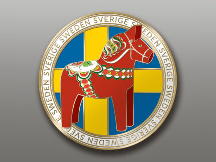 Ett runt emblem föreställer en röd dalahäst med mönster på en gul och blå svensk flaggbakgrund, kantad av ”SWEDEN SVERIGE” i guld på vitt. Produkt: Husky, liggande 25 cm.